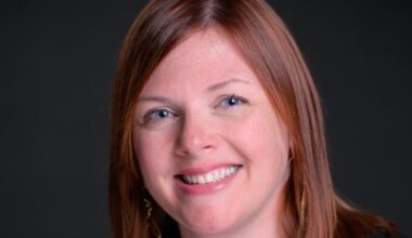 Headshot of Amie Hendrix, a woman with auburn hair, smiling against a dark background.