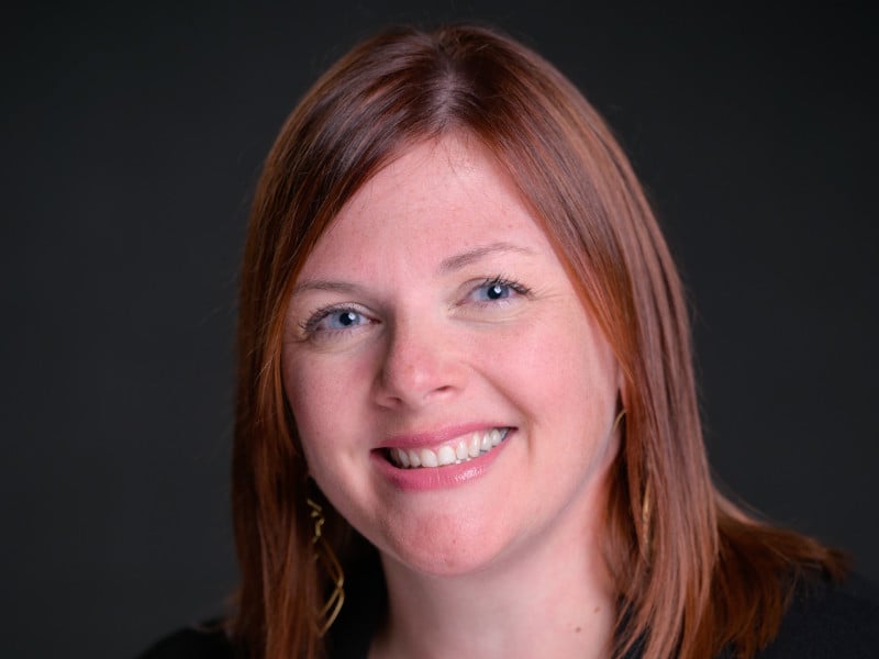 Headshot of Amie Hendrix, a woman with auburn hair, smiling against a dark background.