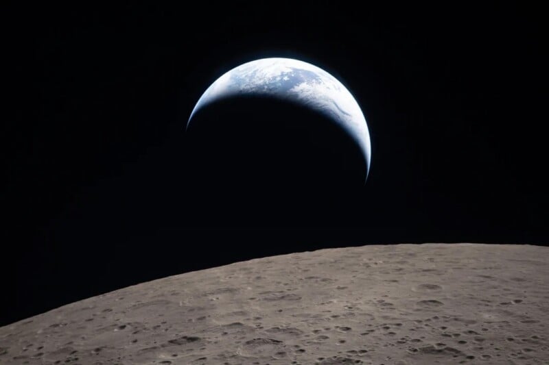A view of the crescent Earth rising above the barren, cratered surface of the Moon, set against the blackness of space.