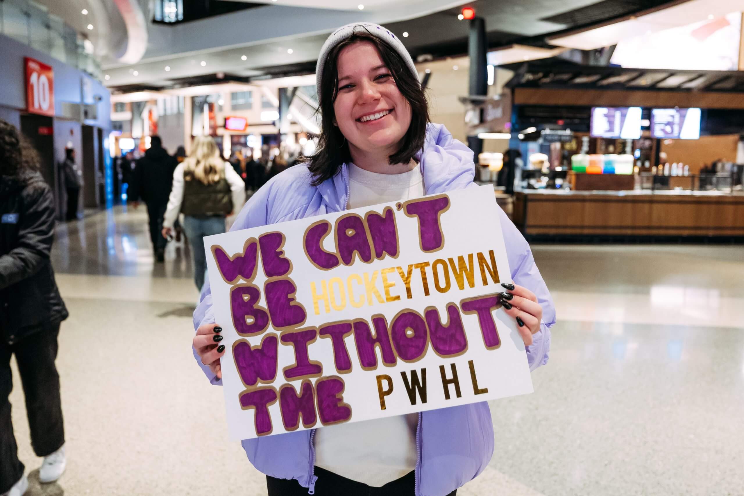A fan holds a sign that reads "We can't be Hockeytown without the PWHL"