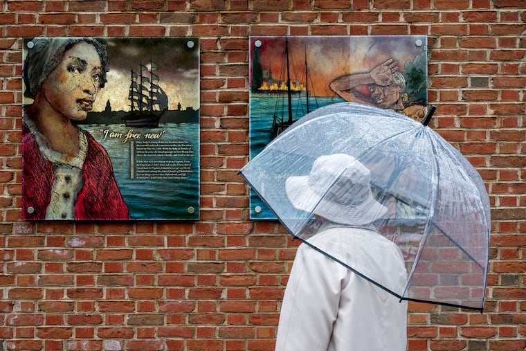 A visitor pauses at a panel about Ona Judge (left) at the President's House Site before community members, advocates, and leaders joined the  Avenging The Ancestors Coalition (ATAC) for their annual gathering honoring Ona Judge’s life, resistance, and enduring impact.