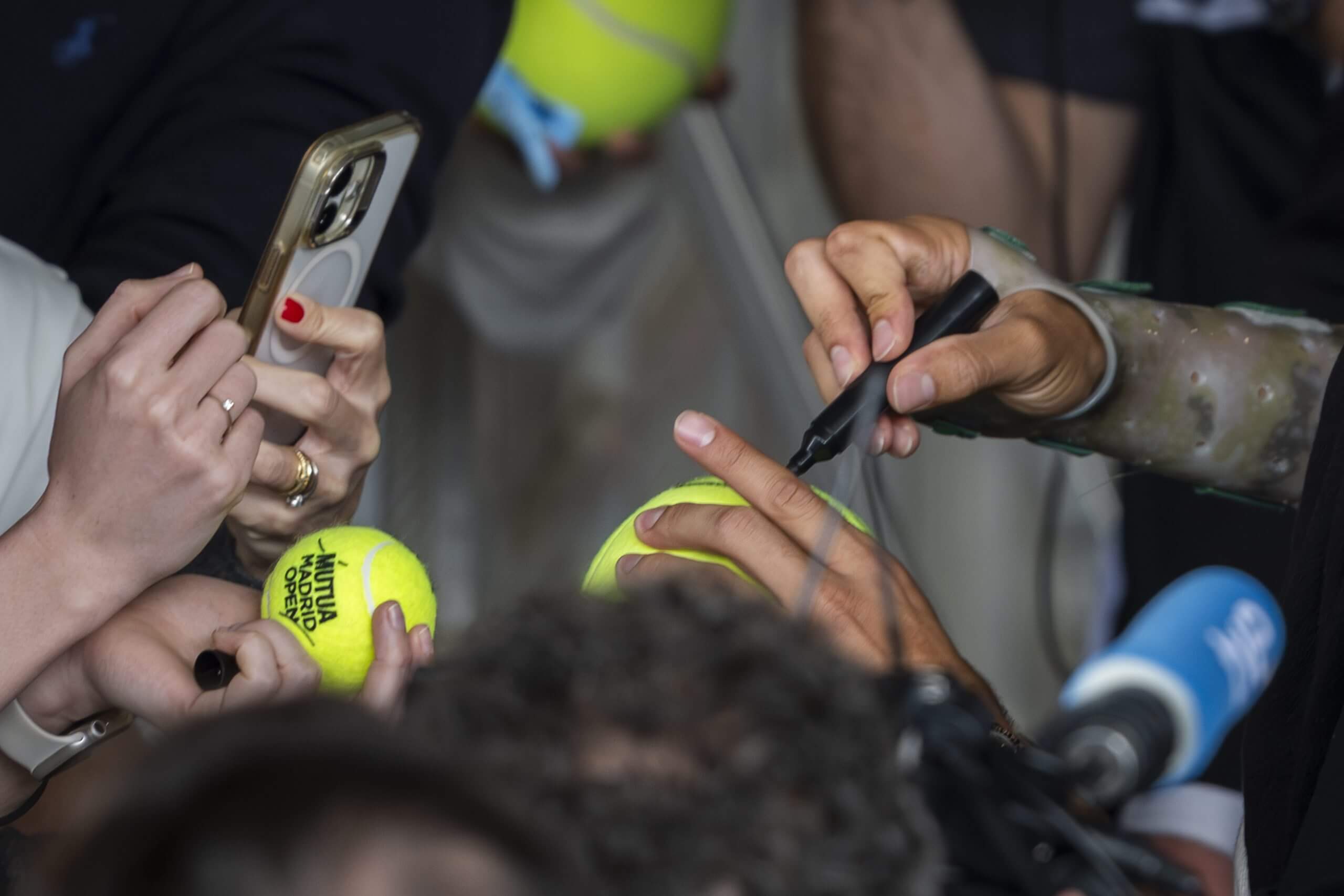 Carlos Alcaraz (out of shot) signs a tennis ball with his right hand, with his wrist in a splint.