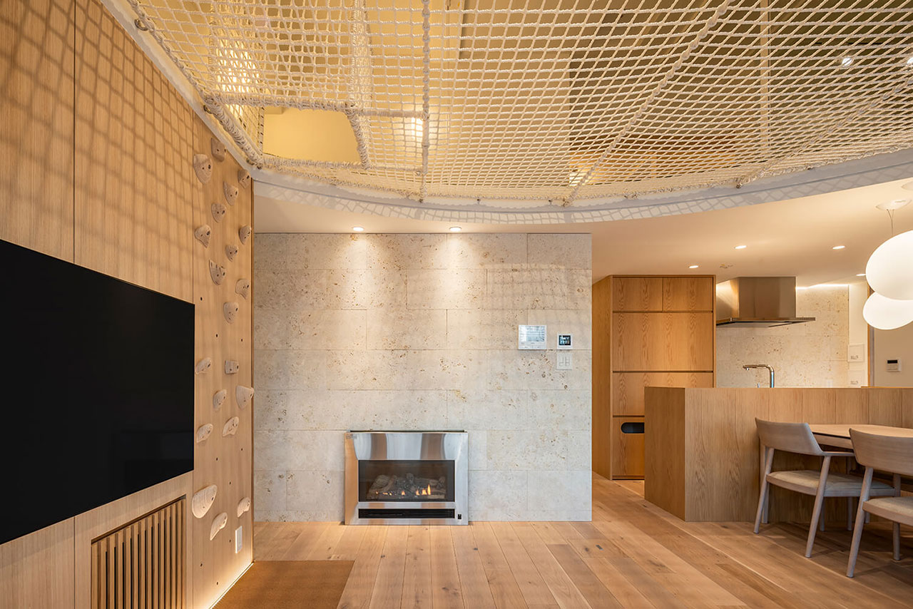 Modern living space with a climbing wall, fireplace, wooden furniture, open kitchen, and a suspended net ceiling.