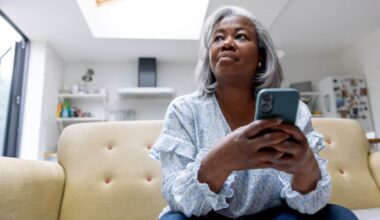 Mature black woman at home texting on her cell phone while sitting on the couch