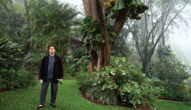 Man in a garden holding a water bottle, surrounded by lush green plants and trees on a misty day.