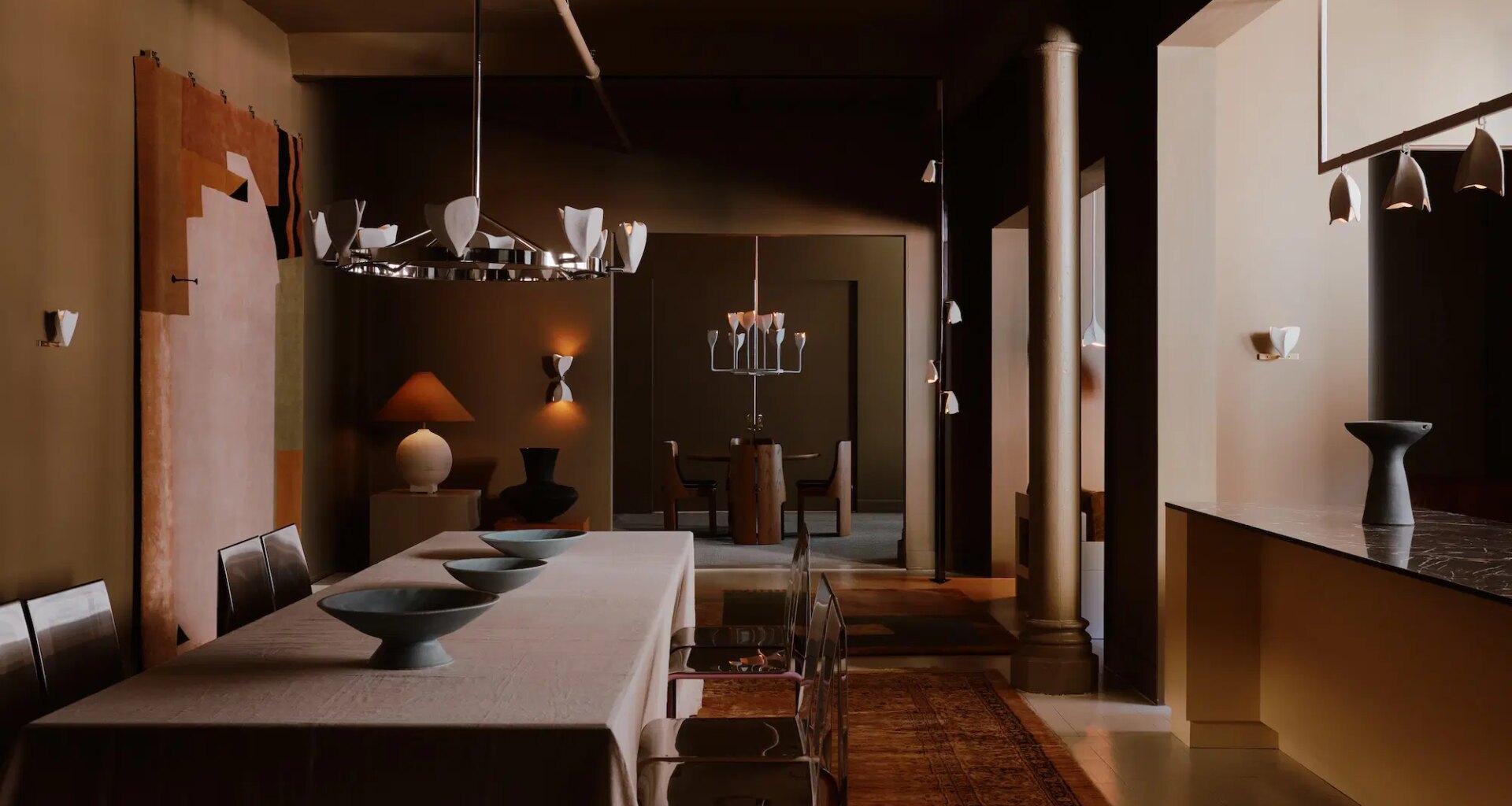 Dimly lit dining room with modern decor, long table, metal chairs, and unique lighting fixtures.