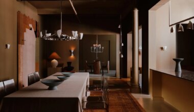 Dimly lit dining room with modern decor, long table, metal chairs, and unique lighting fixtures.