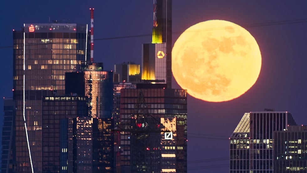 The full moon rises behind the buildings of the banking district in Frankfurt, Germany,...