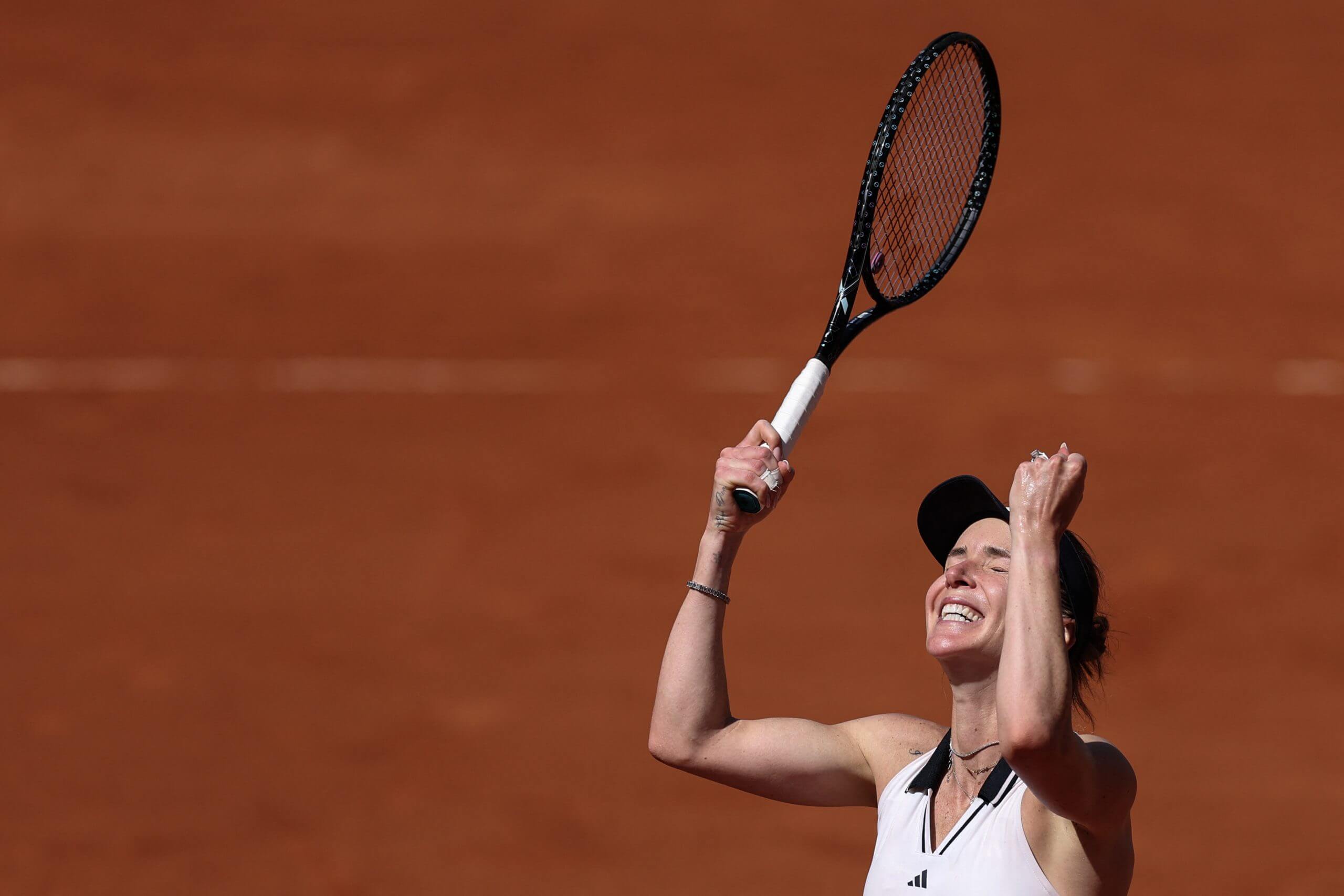Elina Svitolina raises her racket and arms in celebration on a clay tennis court.