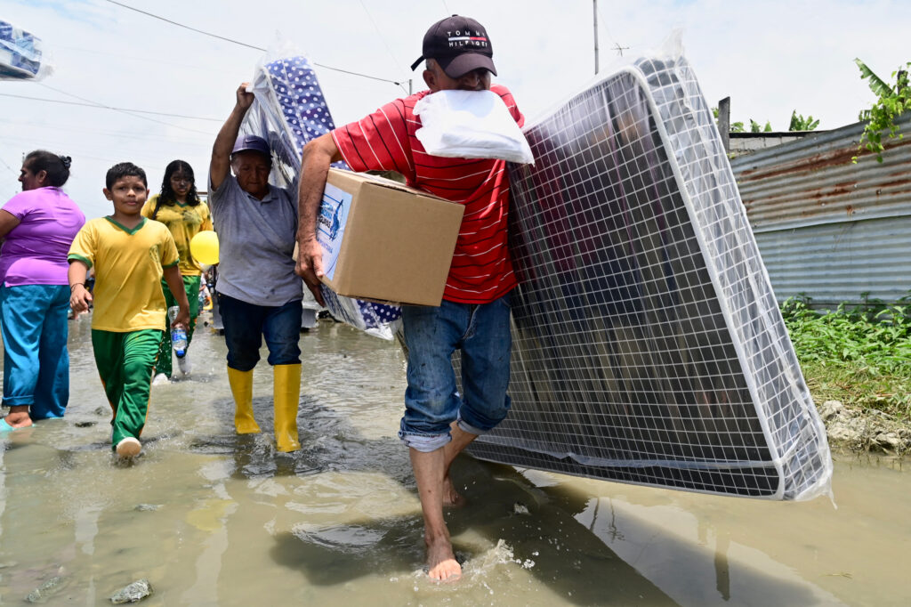 People carry their belongings as they evacuate due to flooding in Yaguachi, Ecuador, on Feb. 25, 2025. Credit: Marcos Pin/AFP via Getty Images