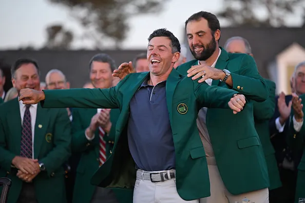 Rory McIlroy of Northern Ireland is awarded the green jacket by Scottie Scheffler after winning the Masters in 2025.