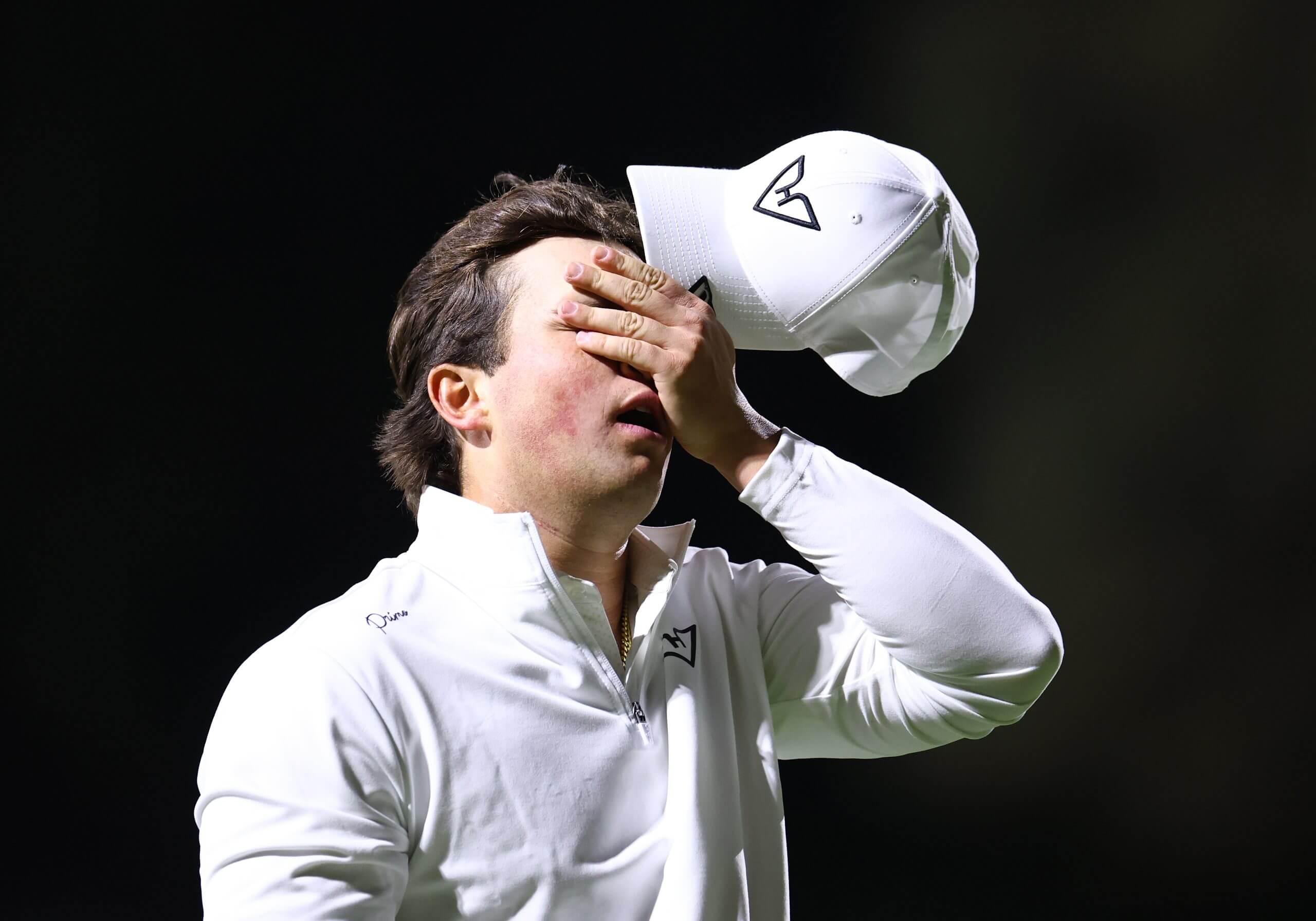 Michael La Sasso holds his left hand over his eyes while also holding his ball cap. 
