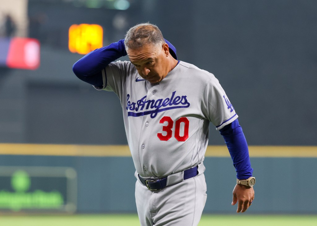 A baseball coach in a grey Los Angeles jersey looking down with his hand on the back of his neck.