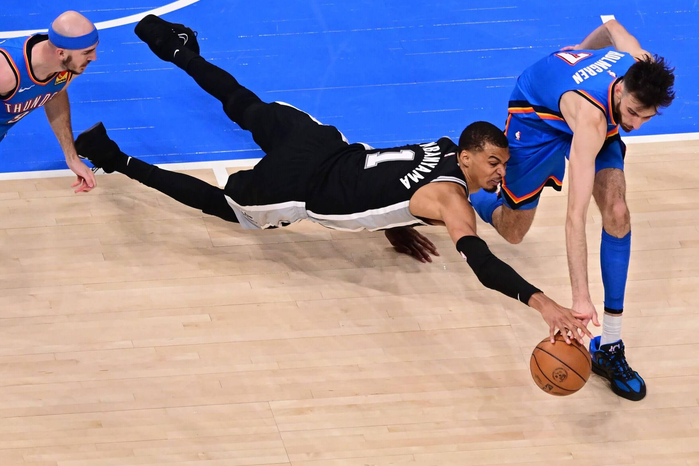 San Antonio's Victor Wembanyama dives for the ball alongside Oklahoma City's Chet Holmgren (7) and Alex Caruso.