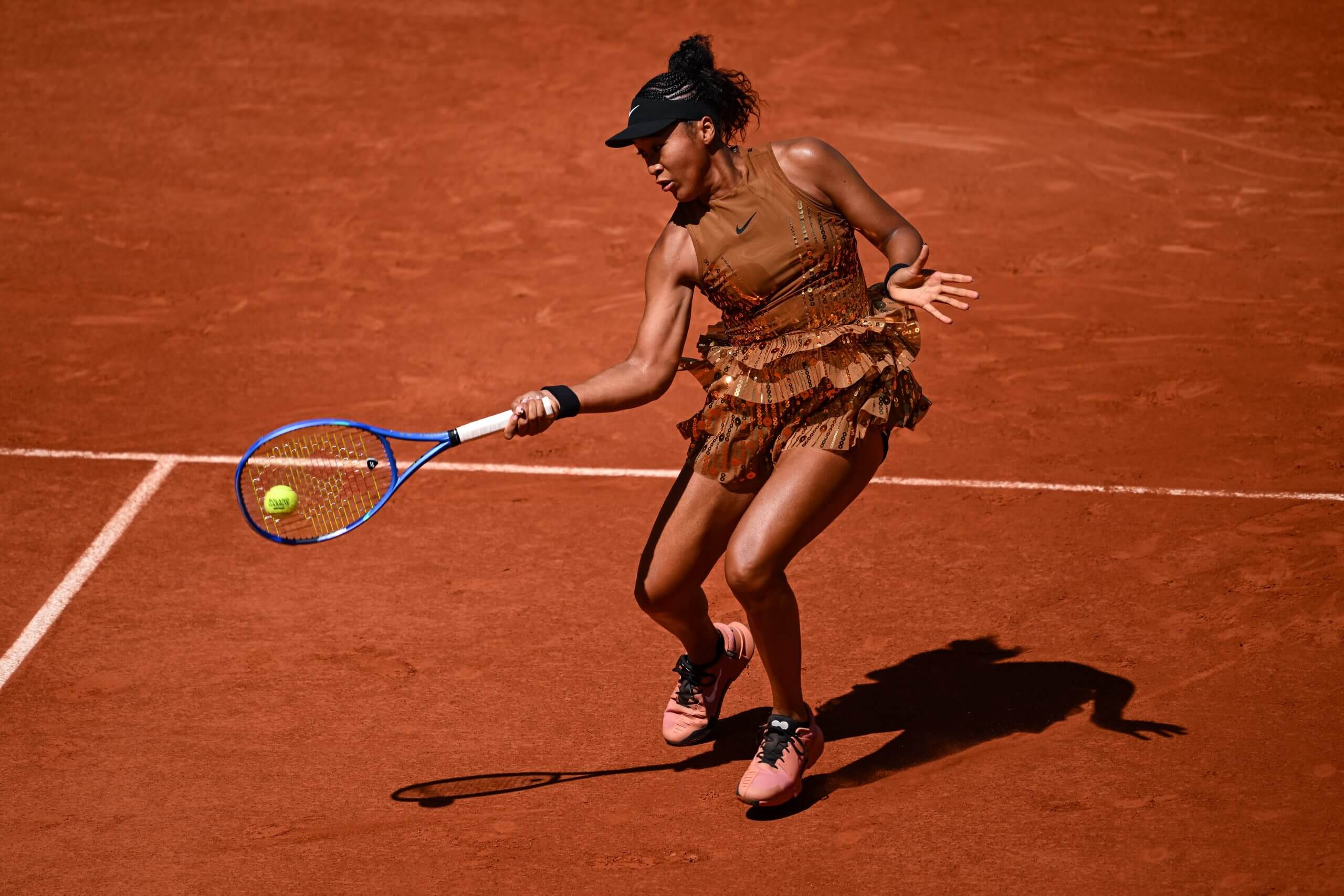 Naomi Osaka hits a forehand wearing a gold tennis dress.