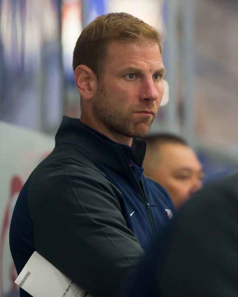 A man with light brown hair and a beard, wearing a dark athletic jacket, looks intently to the right.