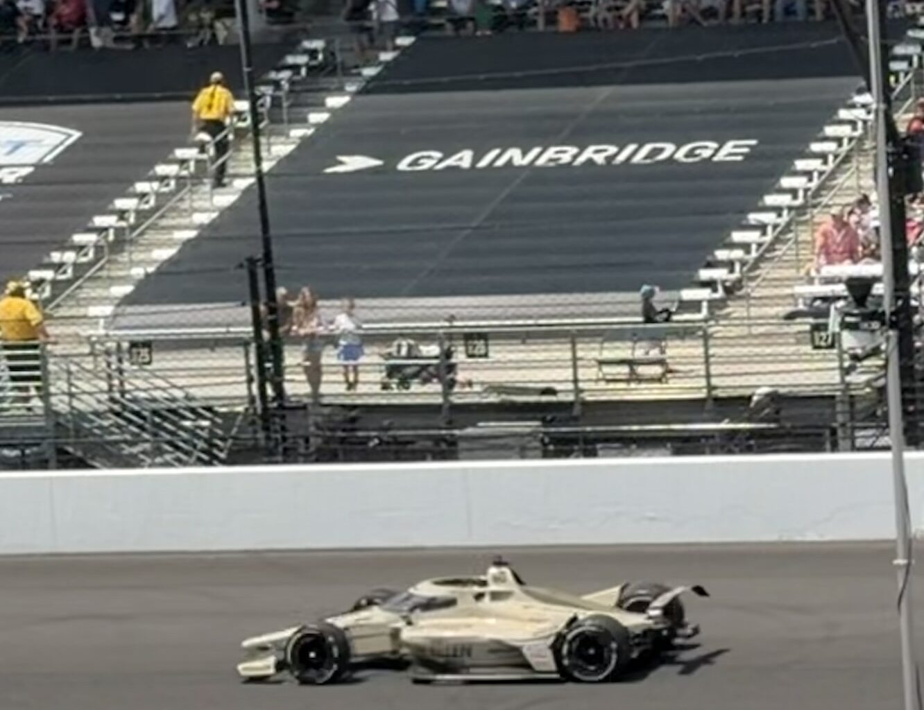 Race car on a track with spectators in the stands; 'GAINBRIDGE' painted on the surface ahead of the car.