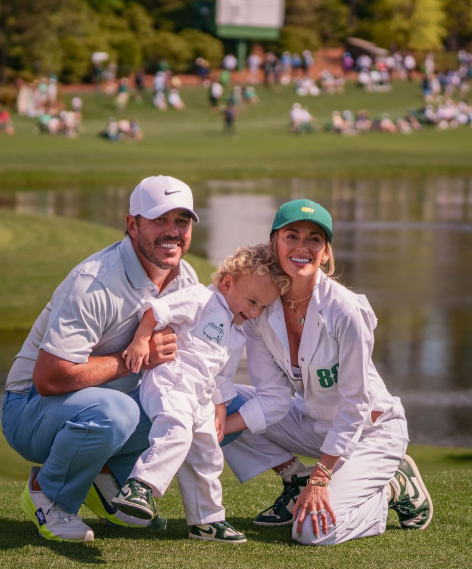 Brooks Koepka, his wife, and child posing on a golf course.