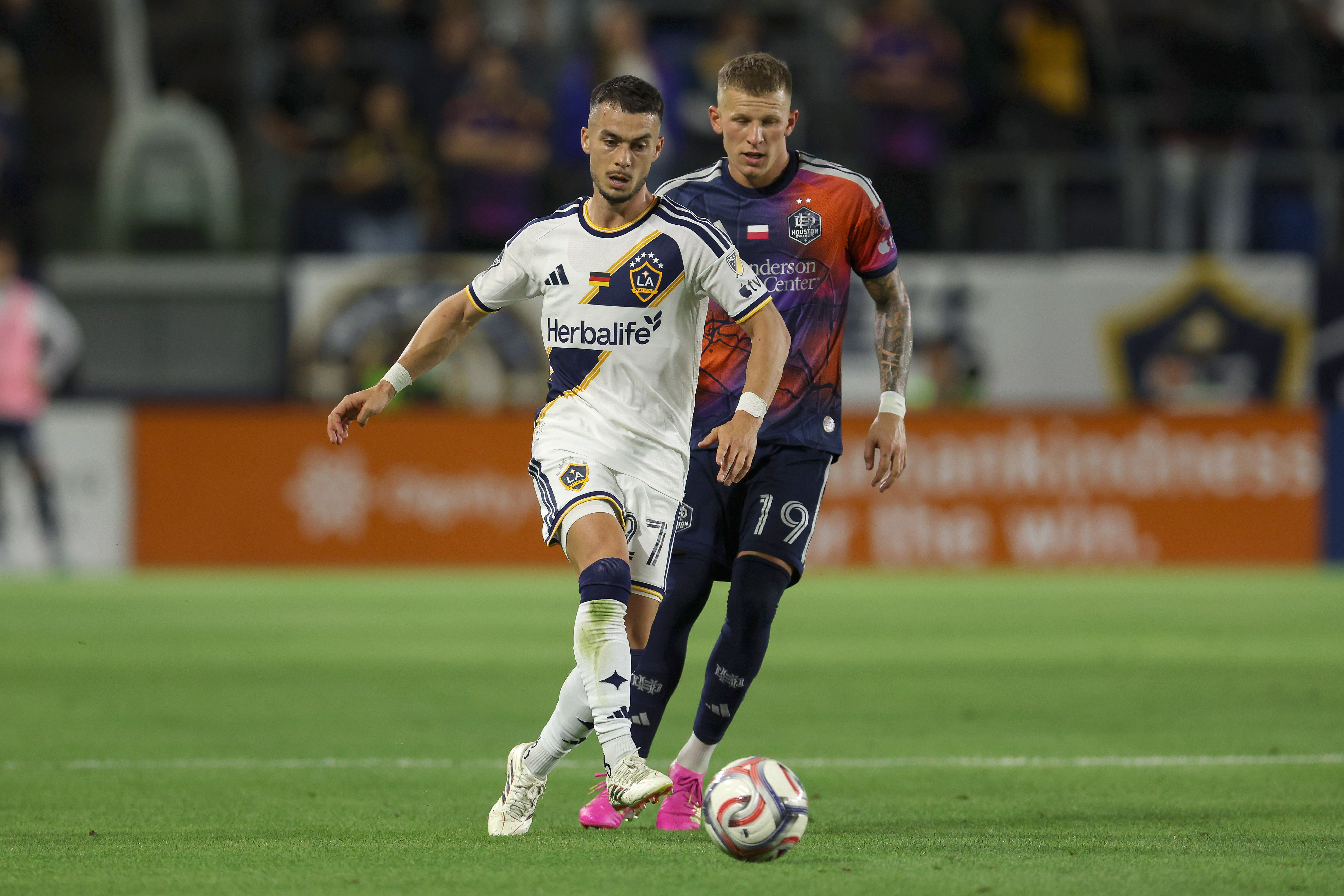 Galaxy midfielder Erik Thommy, front, kicks the ball defended by...