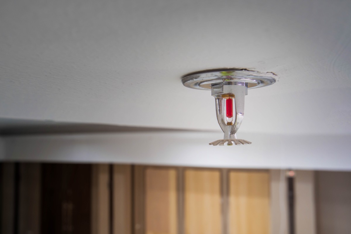 Close-up of a small recessed ceiling light fixture mounted to a white ceiling, showing metal housing and a red inner component.