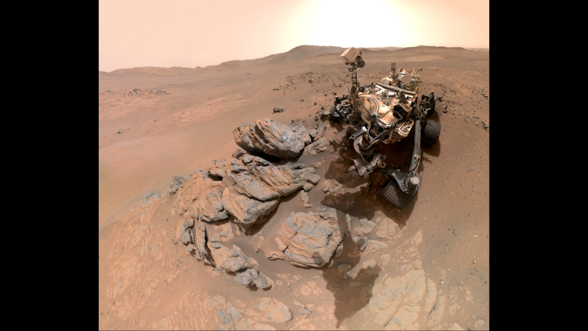 A metal-looking rover with four wheels in an arid, red-brown landscape.