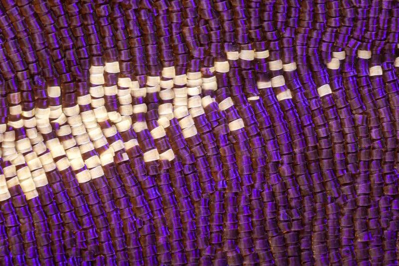 Close-up of purple and gold sequins arranged in a wave-like pattern, creating a shimmering and textured surface with reflective light.