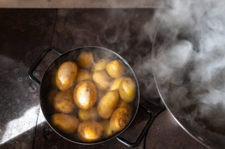 Close-up view of a pot filled with boiling potatoes, releasing steam as they cook on a rustic stove. The natural lighting and traditional setup add a homely and authentic touch, evoking the warmth of homemade cooking. Perfect for themes of food preparation, rustic kitchens, and traditional cooking methods.
