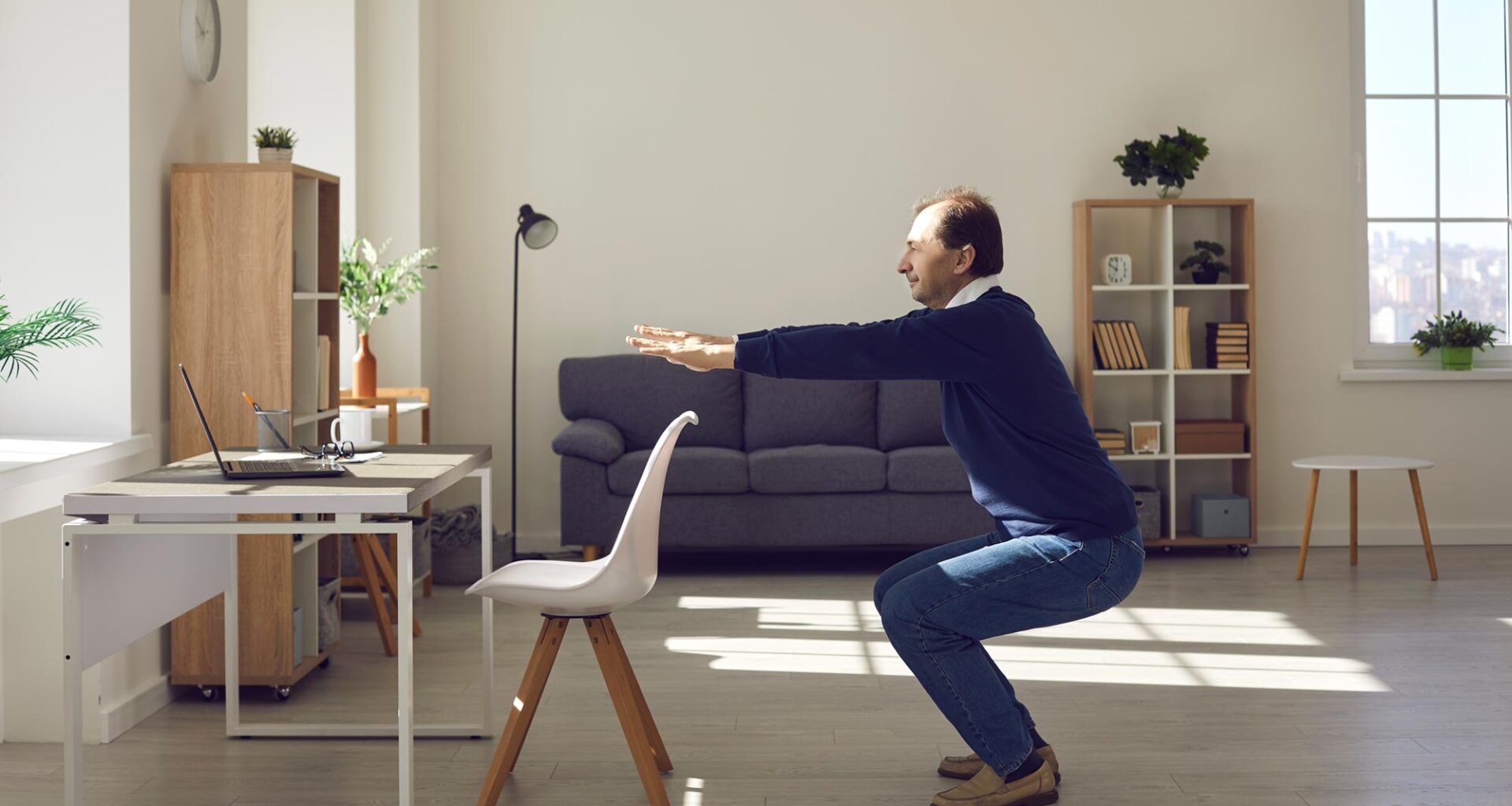 Senior Man Performing Squat Exercise by Desk