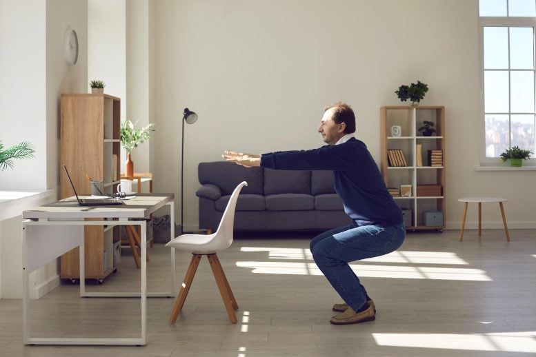 Senior Man Performing Squat Exercise by Desk