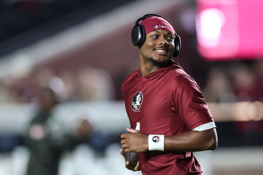 Florida State player smiling, wearing headphones and a maroon shirt, holding a football.