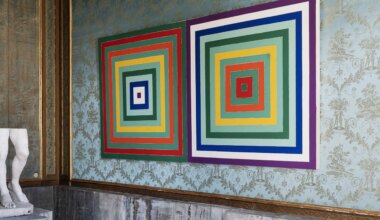 Colorful geometric artwork with concentric squares hangs on an ornate wall next to a partial view of a marble statue.