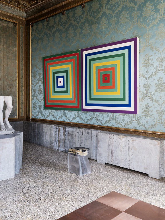 Colorful geometric artwork with concentric squares on ornate wall, statue partial view on the left, modern and classic blend.