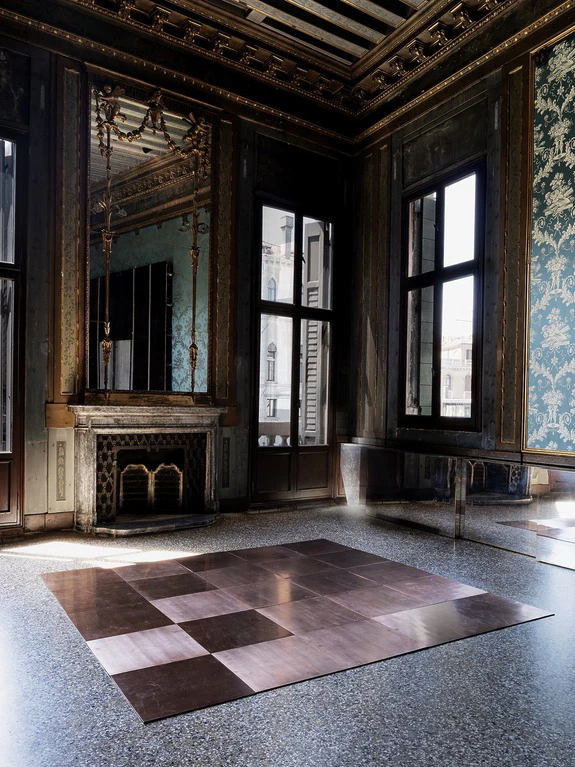 Elegant historical room with ornate mirror, fireplace, large windows, and geometric floor design. Natural light illuminates the space.