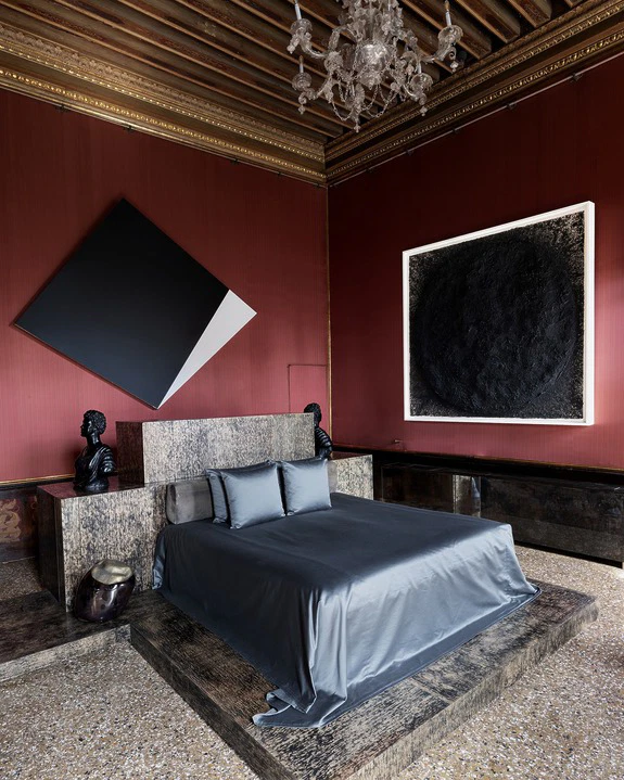 Luxurious bedroom with modern art, featuring a large bed with gray bedding, red walls, and a chandelier.