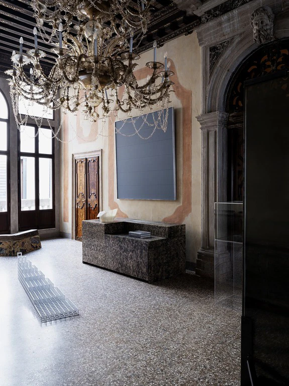 Opulent room with a grand chandelier, modern art, and minimalist furniture in a historic setting.