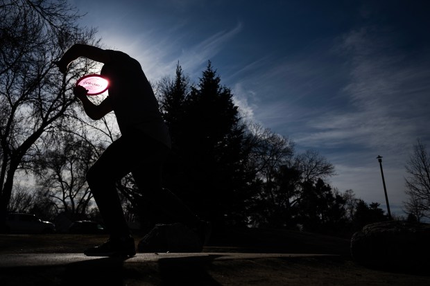 The sun shines through Chris Beach's disc as he fires it from the tee box while disc golfing with friends on Friday, Feb. 6, 2026, at Memorial Park and Johnny Roberts Disc Golf Course in Arvada, Colo. (Photo by Timothy Hurst/The Denver Post)