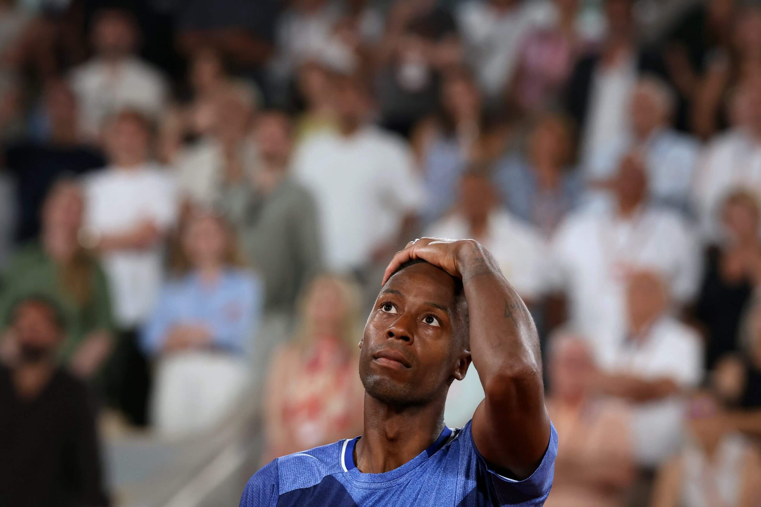 Gaël Monfils puts his hand on his head as he looks up at a crowd in a stadium.