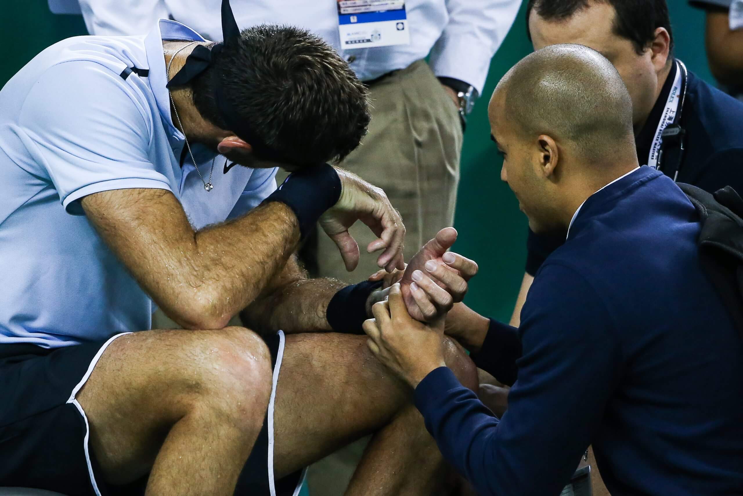 Juan Martín del Potro sits in pain with his head on his right wrist, while a trainer examines his left.