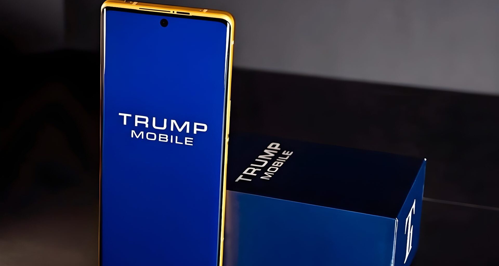 A gold-trimmed smartphone with 'TRUMP MOBILE' displayed on its blue screen stands next to a matching box.