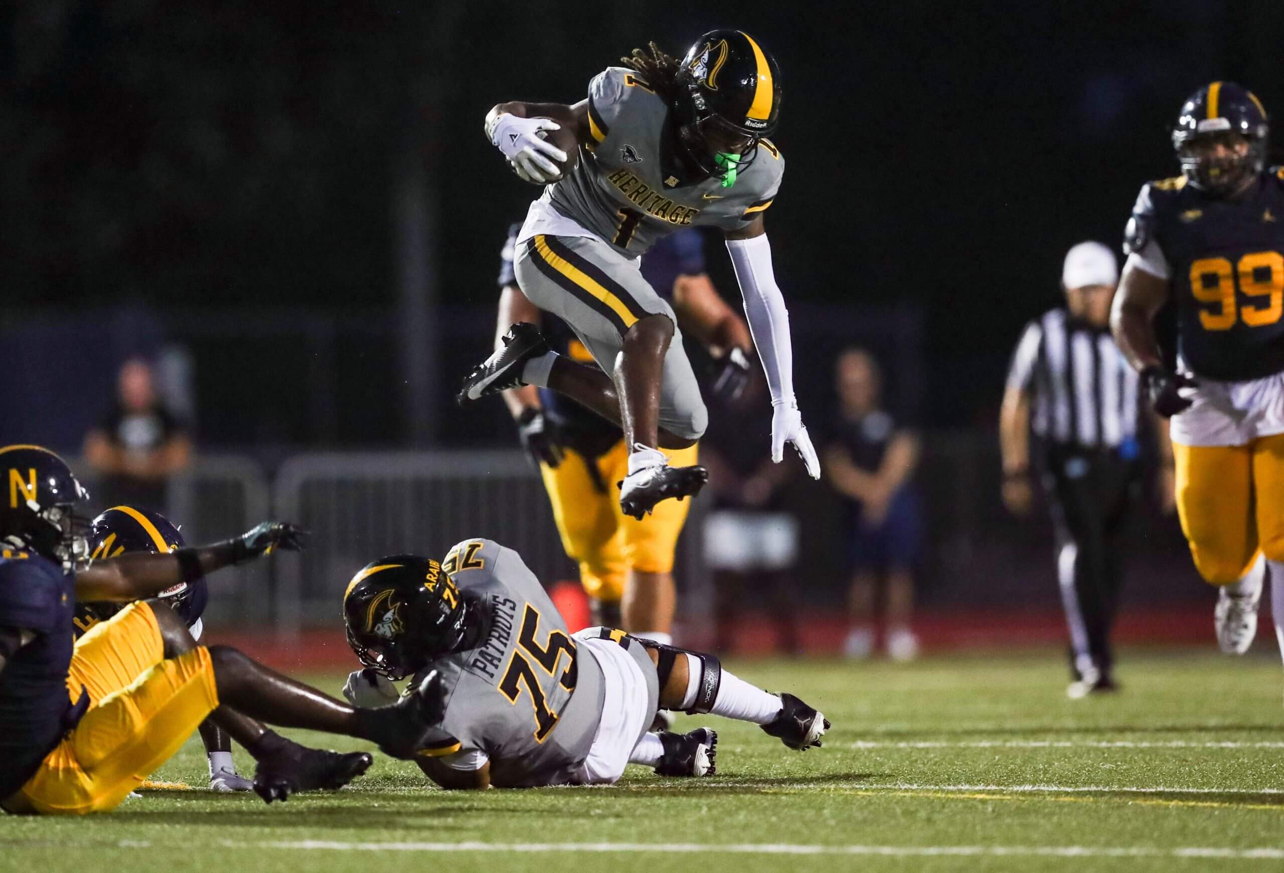 Malachi Toney in an American Heritage uniform hurdles a player on the ground.