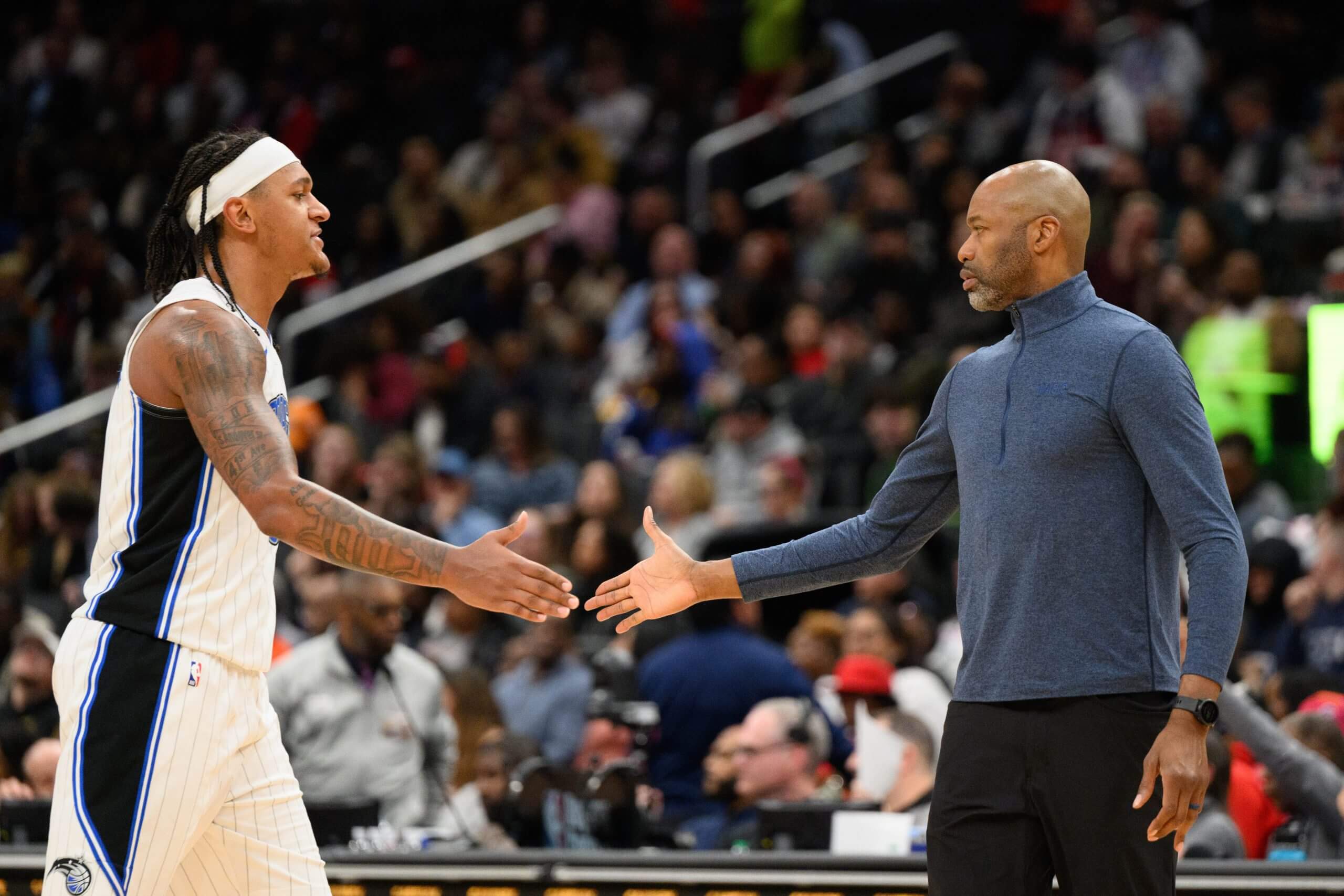 Orlando Magic forward Paolo Banchero walks toward the bench and extends his right hand to slap hands with Orlando coach Jamahl Mosely during an NBA game.