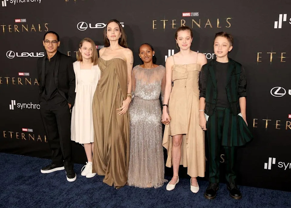 Angelina Jolie and her children at the Eternals premiere, standing together on a blue carpet.