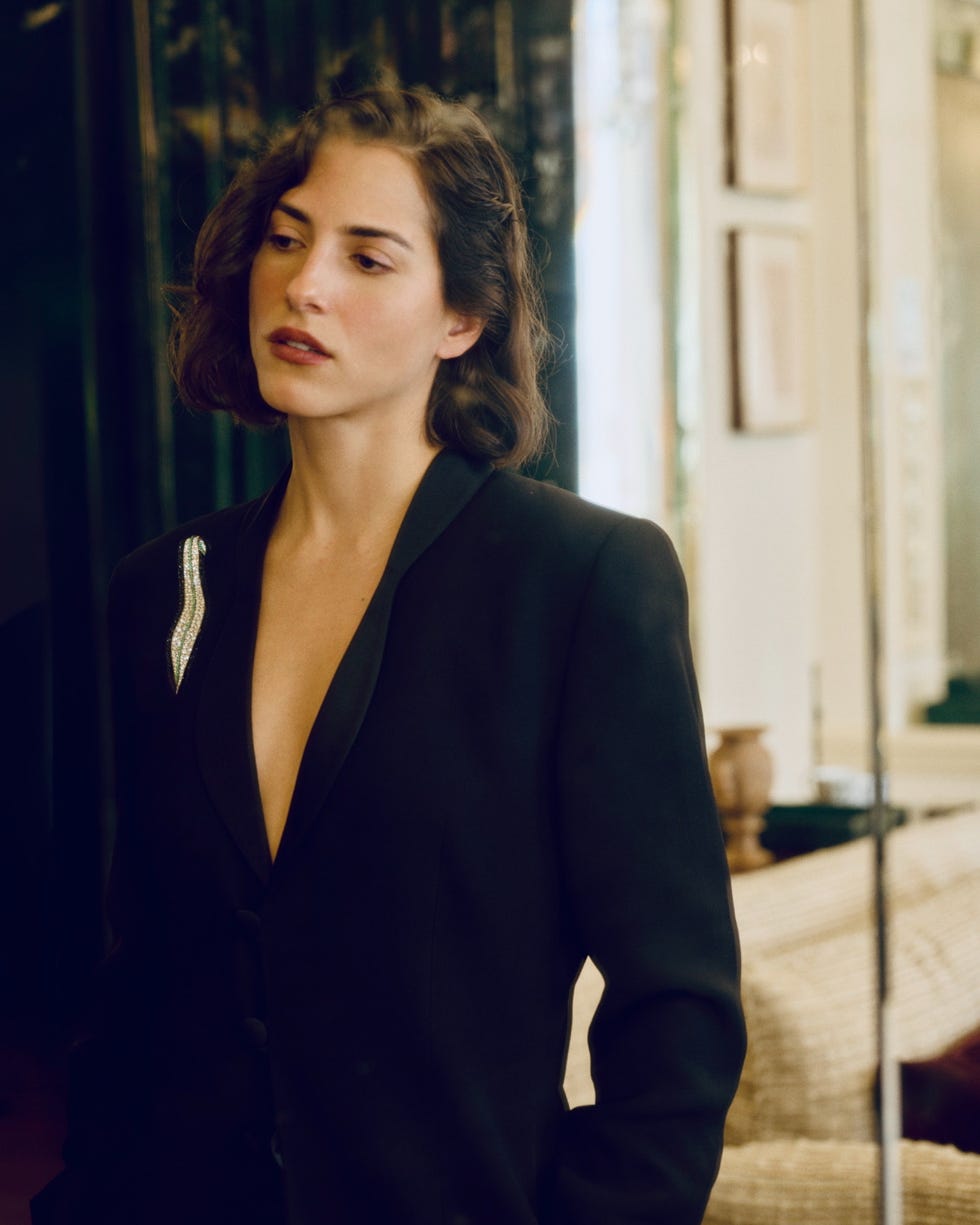 Person wearing a black blazer with a decorative element, standing in a stylish interior.