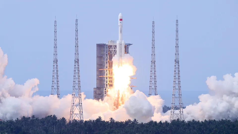 A photo of a Long March 7 rocket lifting off from a forest in China during the day