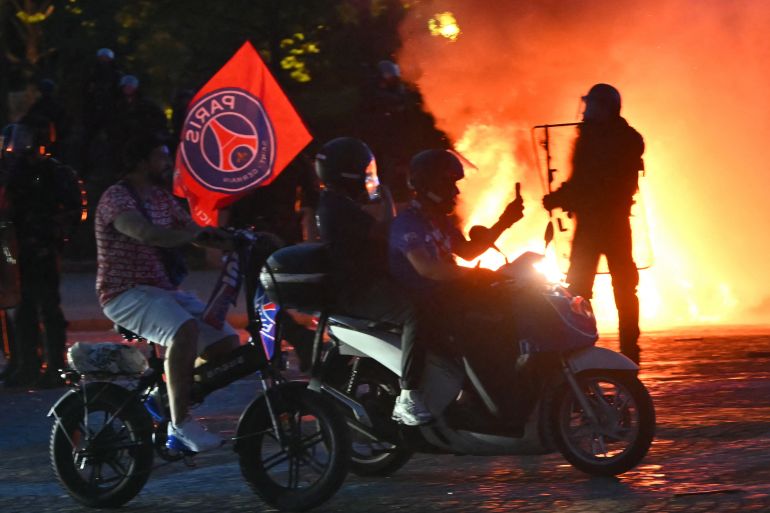 PSG supporters drive their scooters past anti-riot police officers (Rear R) as they celebrate their team's win in the UEFA Champions League final between Paris Saint-Germain (PSG) and Arsenal FC played in Budapest, at Place du Trocadero in Paris on May 30, 2026.