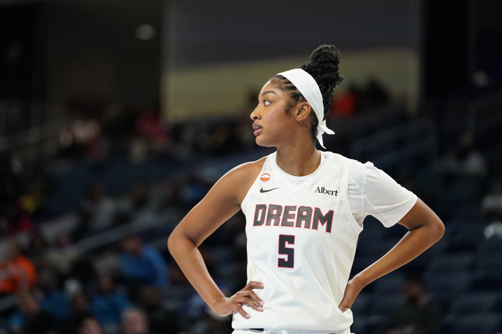 Angel Reese in an Atlanta Dream jersey, looking on during a game.