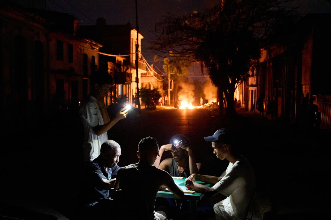 People illuminate themselves with their phones while playing dominoes as a fire set up by residents protesting against prolonged power outages burns on a street in Havana, Cuba, on Thursday, May 14, 2026. (AP Photo/Ramon Espinosa)