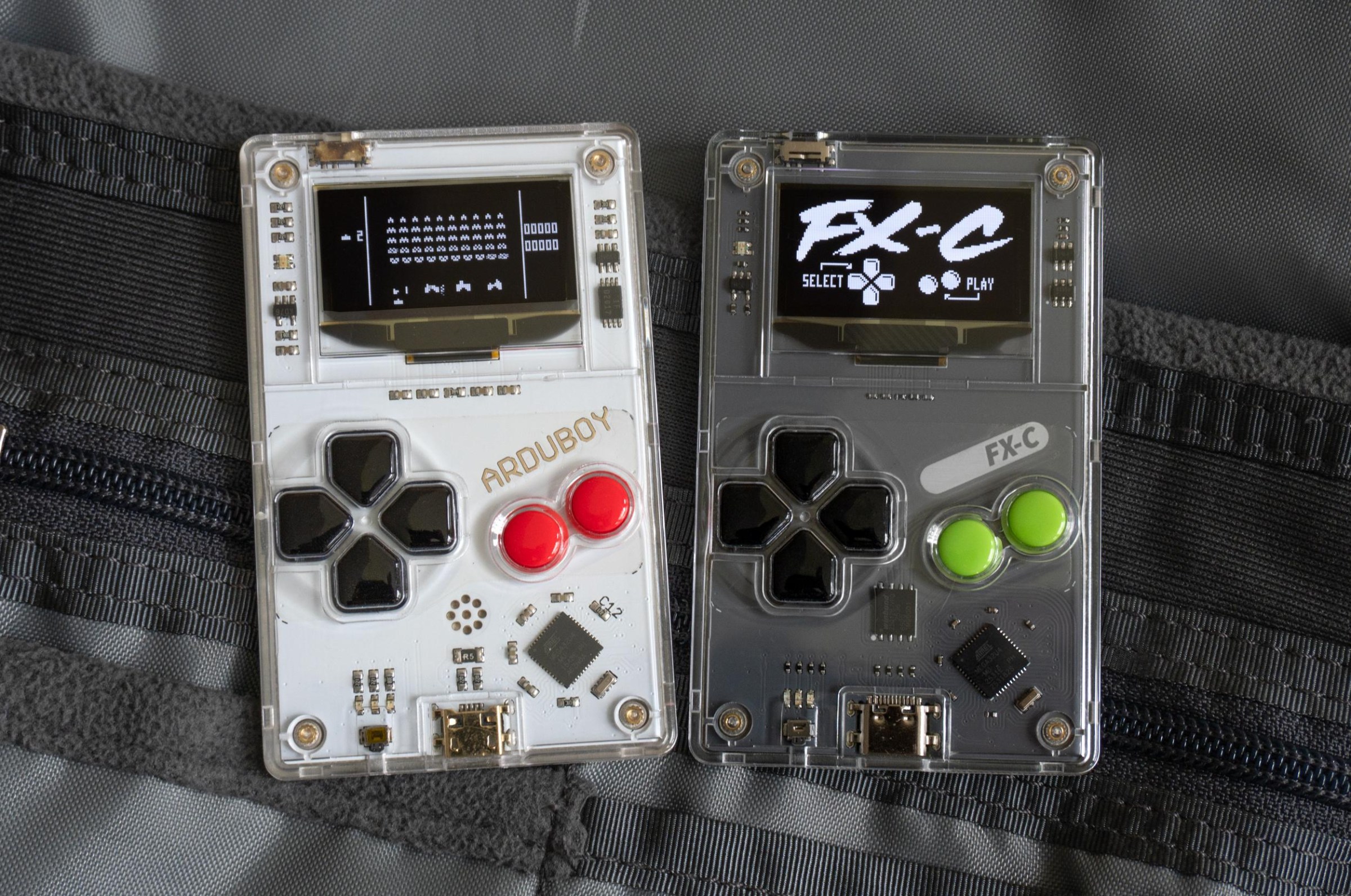 The original Arduboy next to the new Arduboy FX-C sitting on a backpack’s internal pockets.