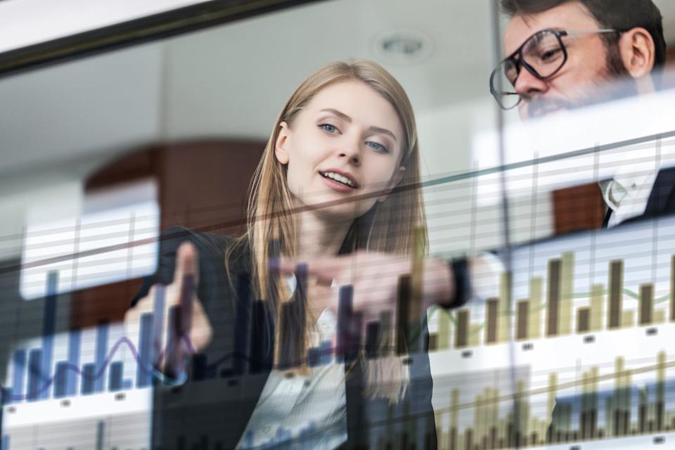 Two people in an office look at data on a transparent screen.