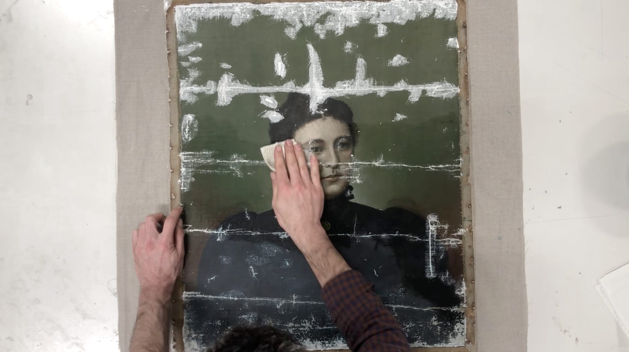 a still from a video by Baumgartner Restoration of a painting being restored, with tears and creases in the canvas being prepped